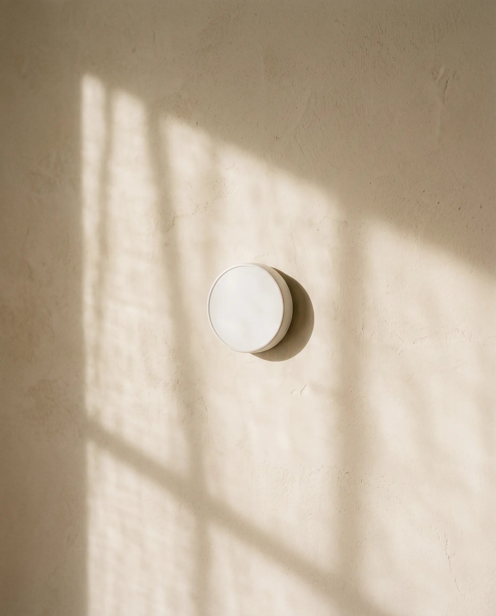 Round thermostat on a cream plaster wall in low winter sunlight